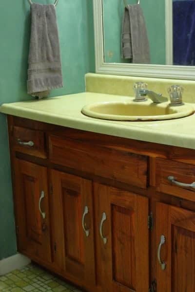 Photo of bathroom vanity with yellow countertop, green wall and wood bathroom cabinet