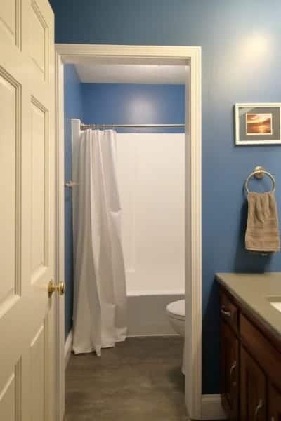 Remodeled 1970s bathroom now has dark blue walls, grey quartz countertop and white plumbing fixtures.