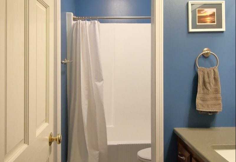 Remodeled 1970s bathroom now has dark blue walls, grey quartz countertop and white plumbing fixtures.
