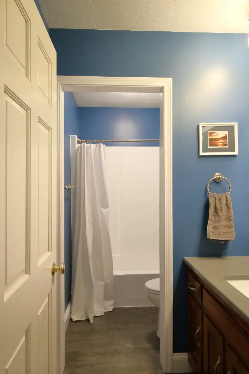 Bathroom remodeling project - after. Dark blue walls, dark grey counter and floor, white tub, sink and toilet.