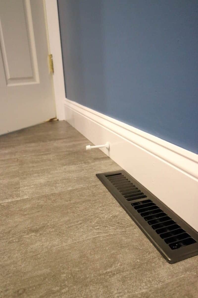 Dark grey luxury vinyl tile, white baseboard and dark blue painted walls.