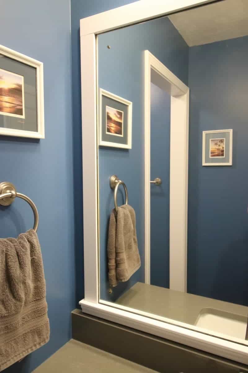 White wood trim around mirror, with a dark grey quartz countertop and dark blue walls complete this bathroom makeover.