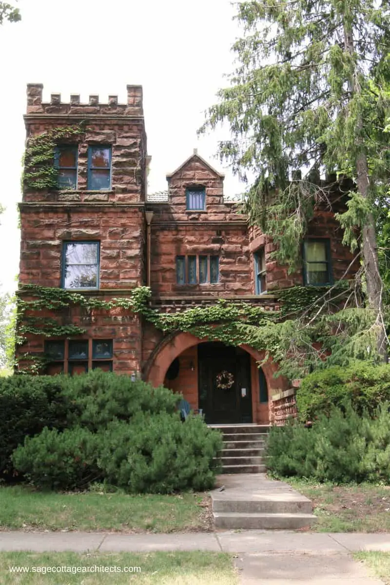 This front elevation of red stone masonry walls with large arch over entry is typical of Richardsonian Romanesque homes.