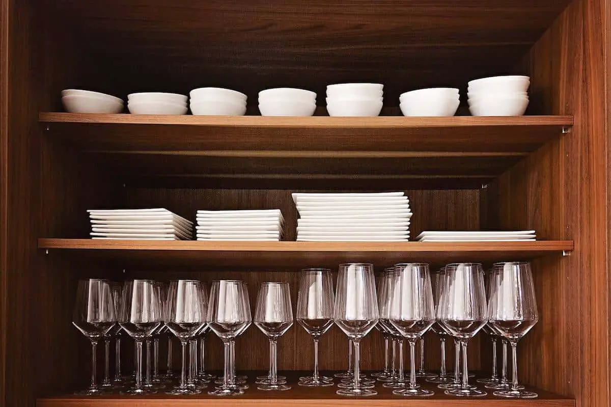 Wooden cabinet with white tableware and wine glasses