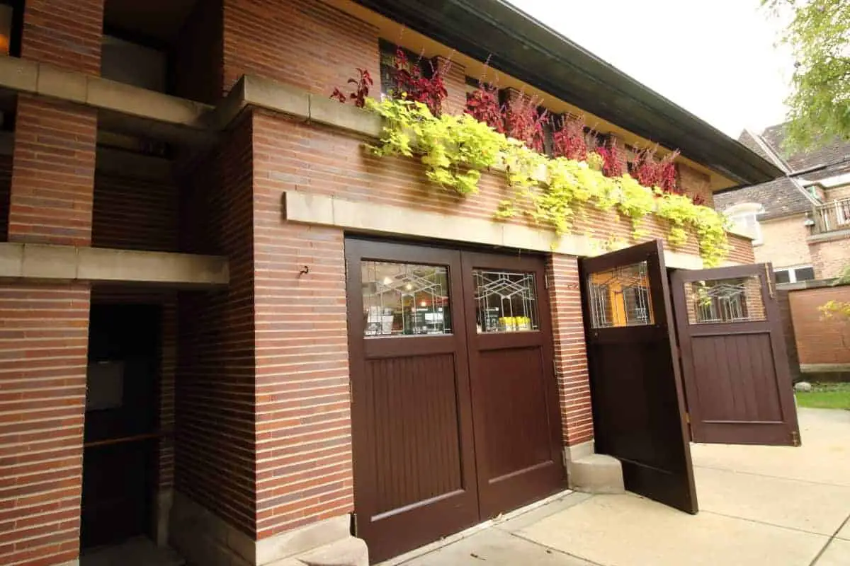 Garage front of Prairie style home with red brick, limestone banding, and dark brown carriage doors.