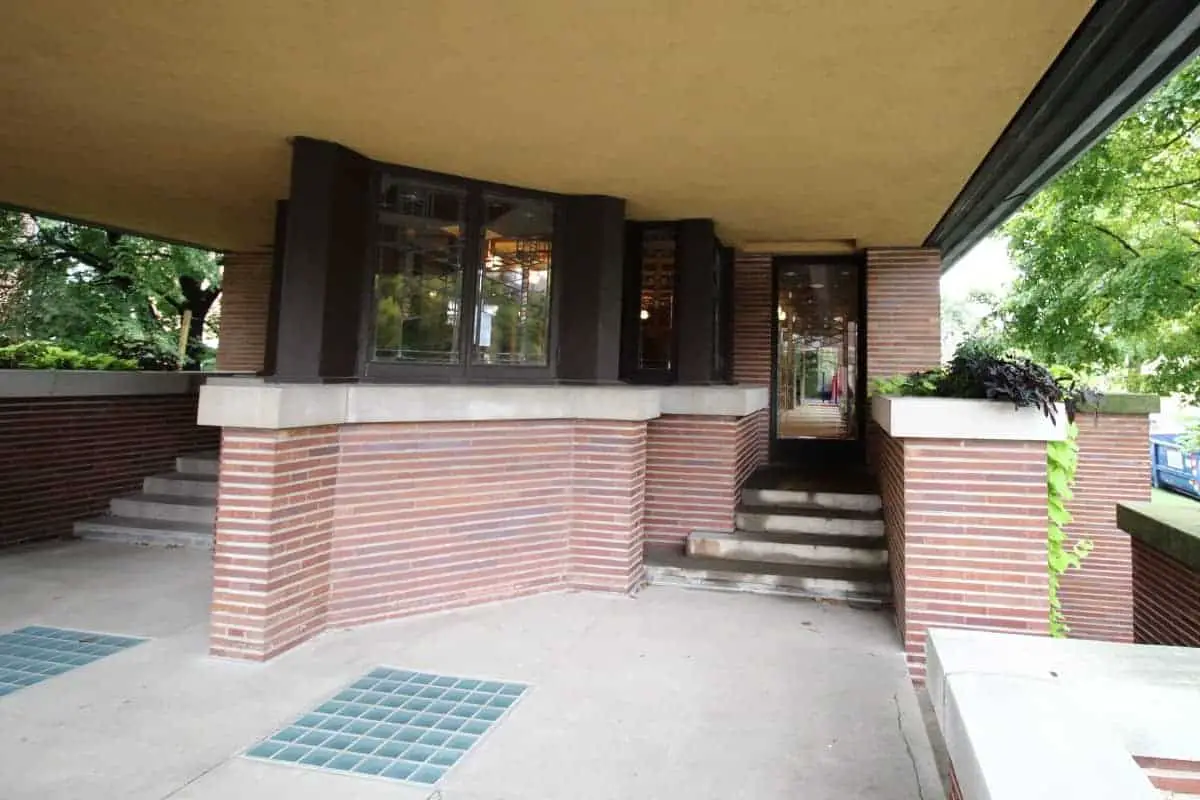 Concrete balcony of a Prairie Style home, with red brick, limestone wall caps, dark window trim, and cream stucco ceiling.