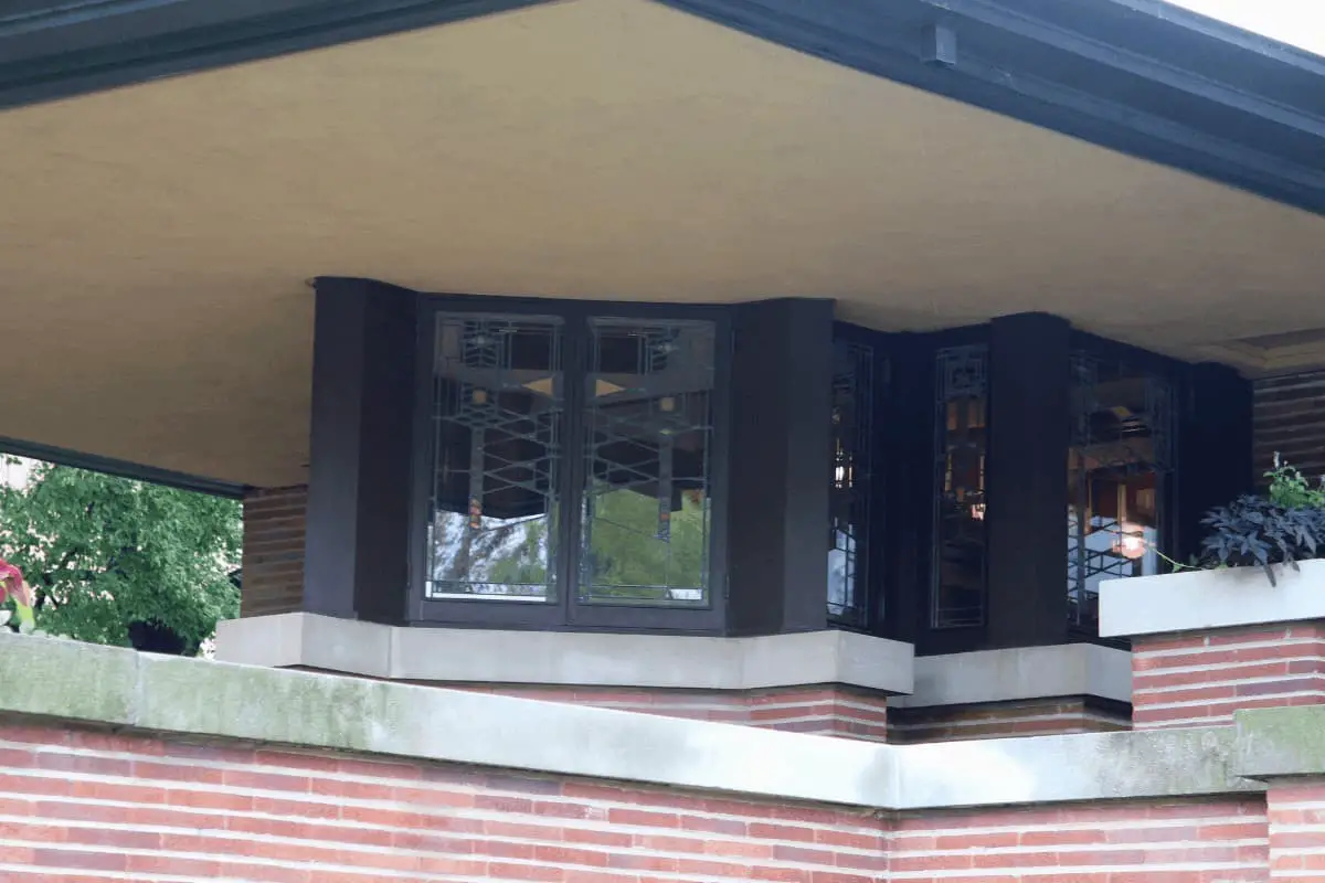 Covered balcony on a Prairie Style home. Red brick, white limestone banding, cream stucco soffit and black window trim.