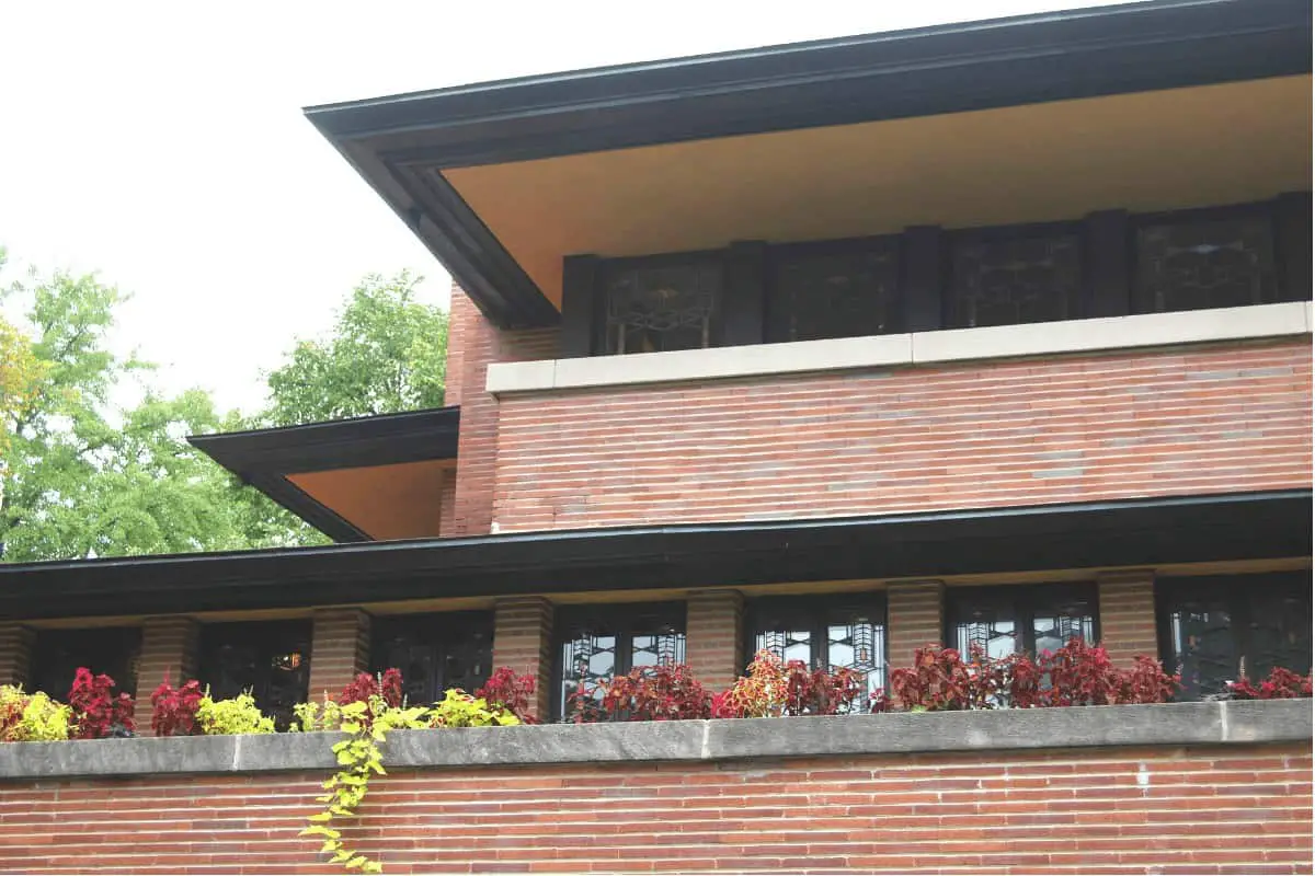 Red brick, white stone banding, and dark eaves on a Prairie Style home.