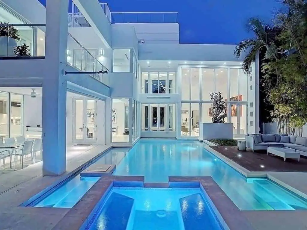 Photo of a white, modern style beach vacation home with a large pool at night. 