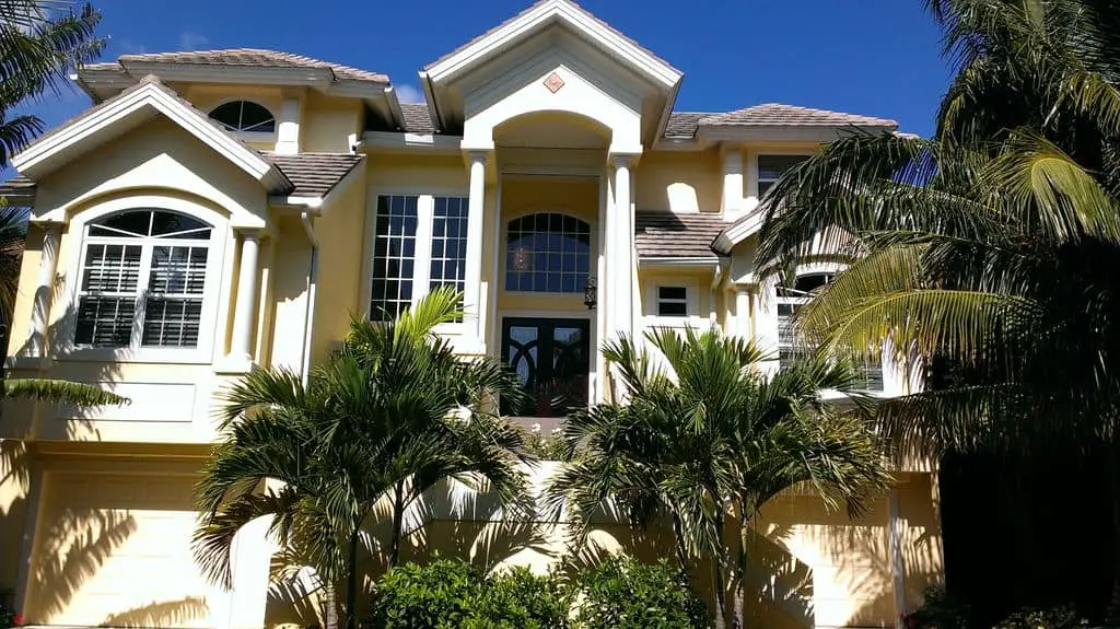 Photo of a yellow and white beach vacation home with palm trees. 