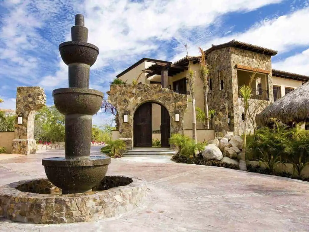 Photo of the entrance to a beach vacation rental home with rustic stone walls and a fountain. 