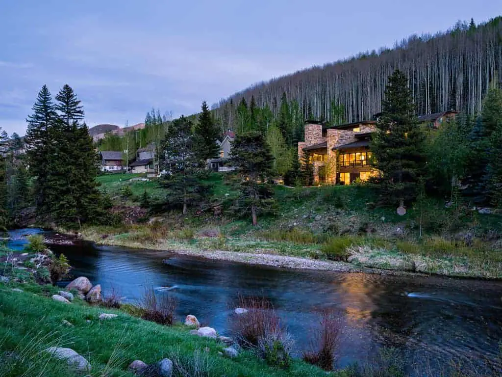 Photo of ski vacation home next to a river, with trees behind. 