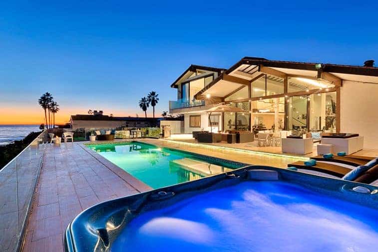 Photo of a beach vacation home at sunset with a large pool and palm trees. 