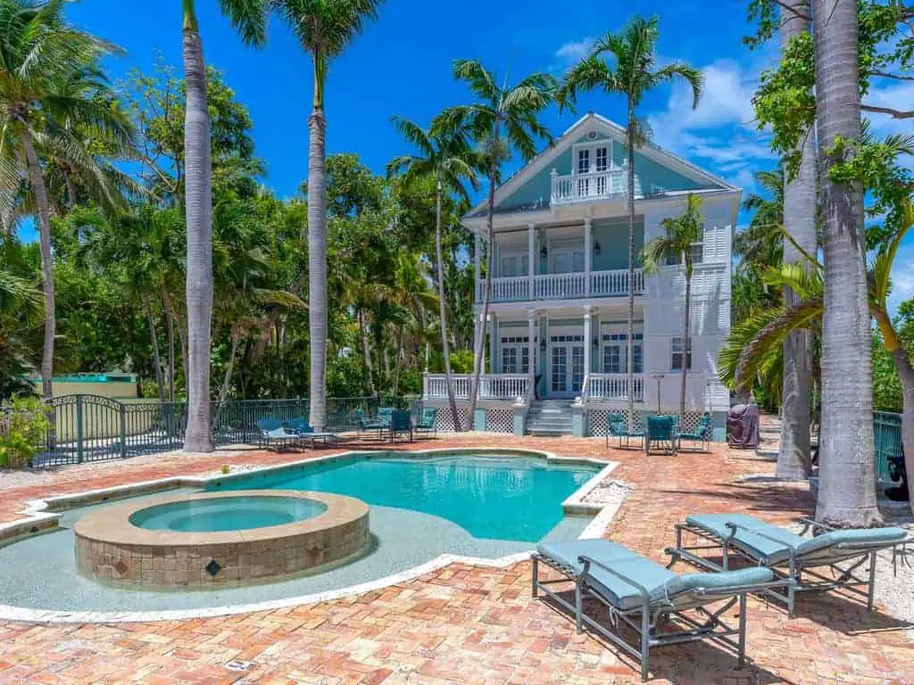 Photo of a beach vacation home in the Key West style with a pool, hot tub and palm trees surrounding it. 