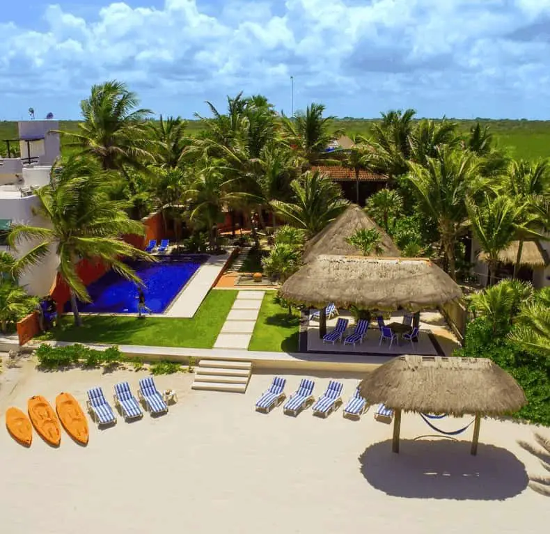 Photo of the ideal beach vacation home. Kayaks, lounge chairs, and thatched shade structures on the beach.