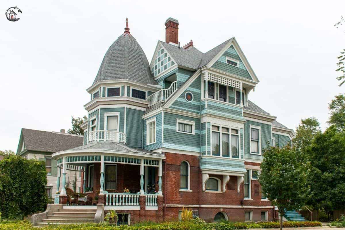 Photo of large Victorian home with round front porch, blue and green color scheme, in a neighborhood of old houses. 