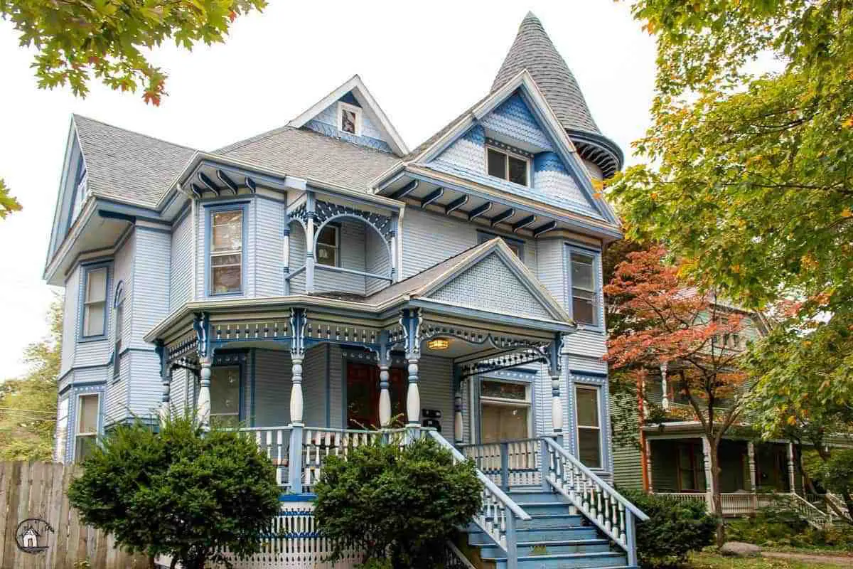 Photo of Victorian home with blue exterior, painted gingerbread and large front porch in a neighborhood filled with old houses. 