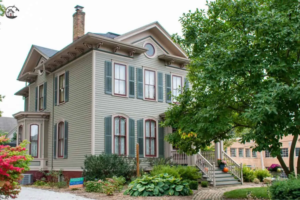 Photo of old house with light green exterior, and dark green shutters.