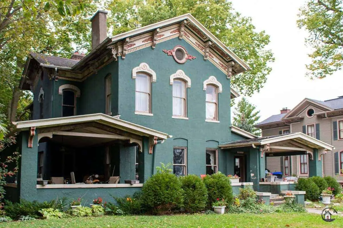Photo of and old house with dark green exterior and large porches.