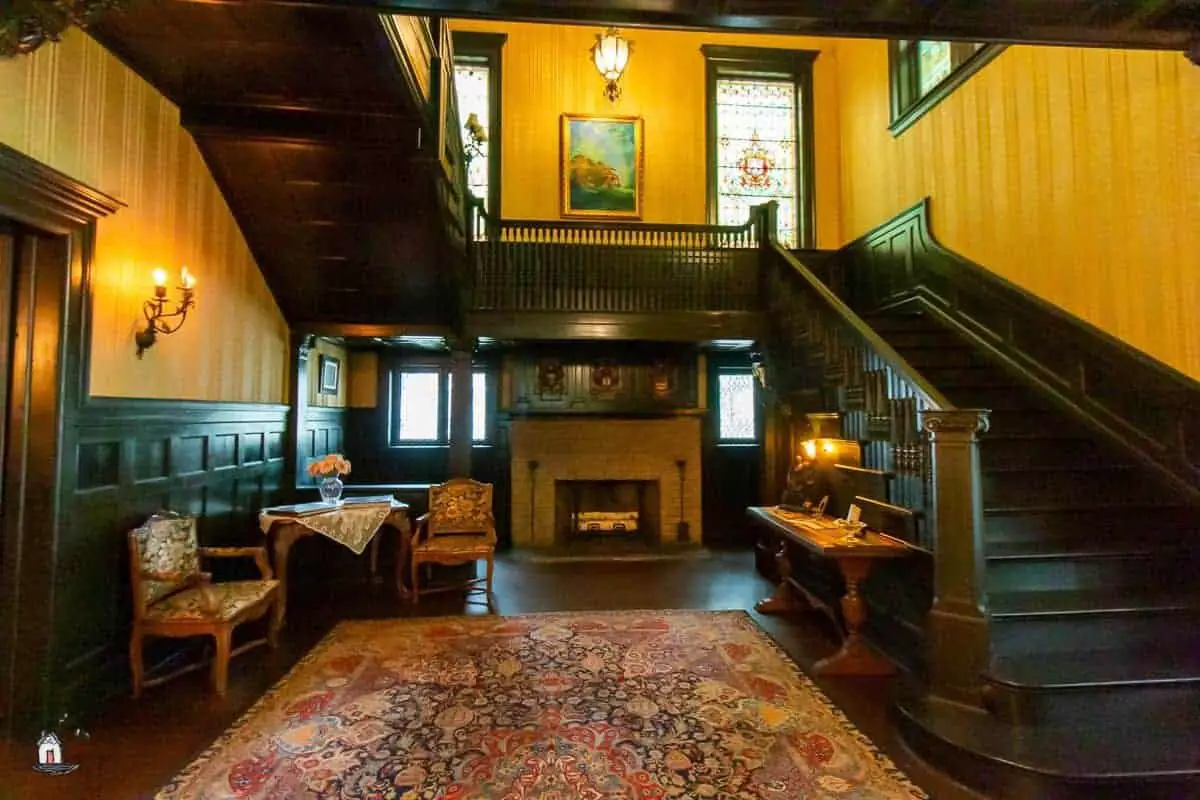 Photo of the interior of the Vrooman Mansion with dark stairs, fireplace, and large stained glass windows. 