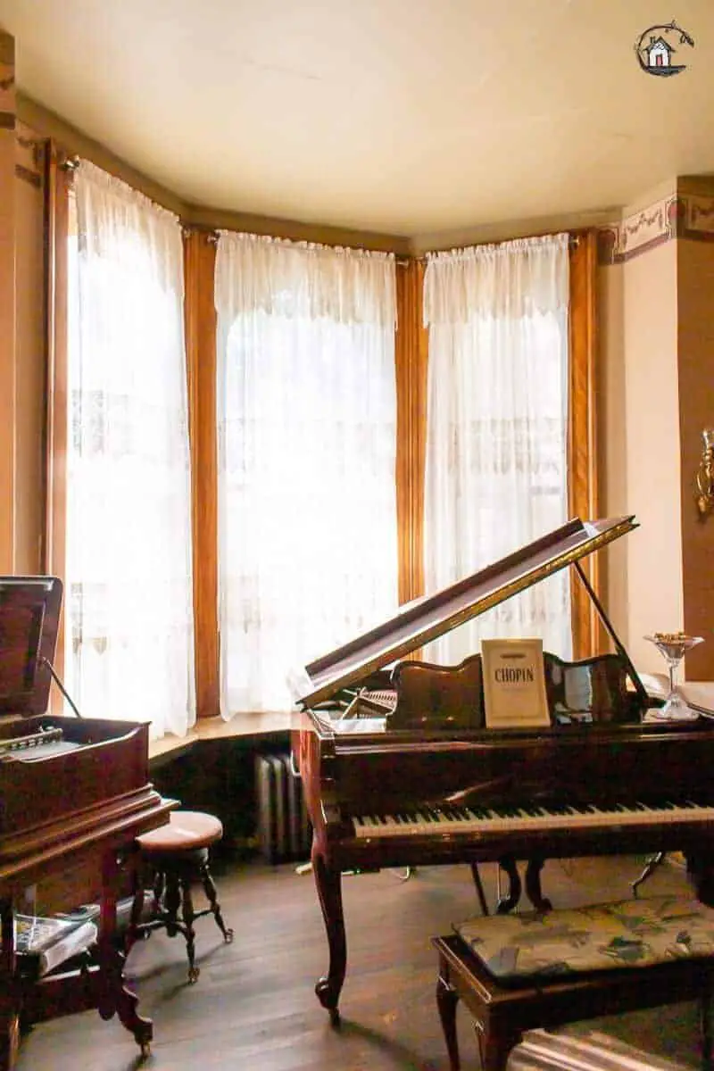 Photo of the Music Room with large windows and grand piano in the Vrooman Mansion. 