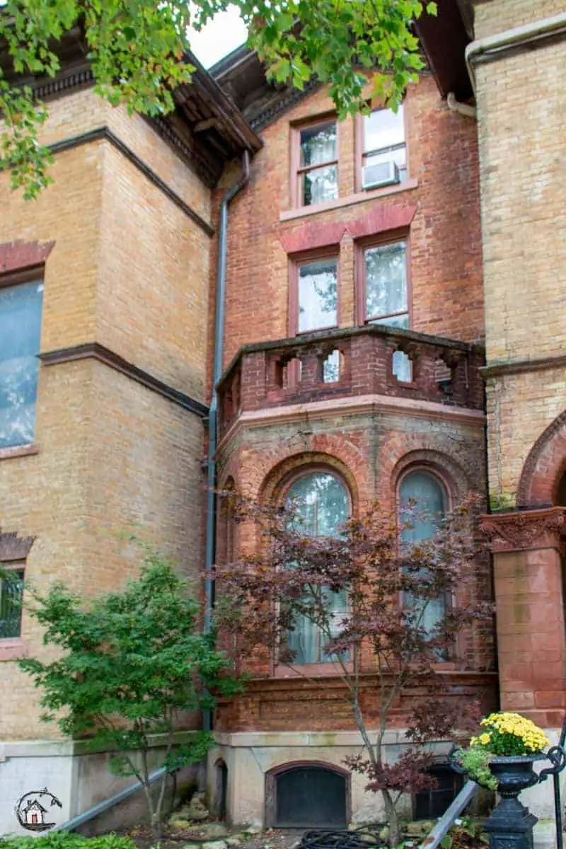 Photo of red brick bay with arched windows, flanked by yellow brick walls on the Vrooman Mansion. 