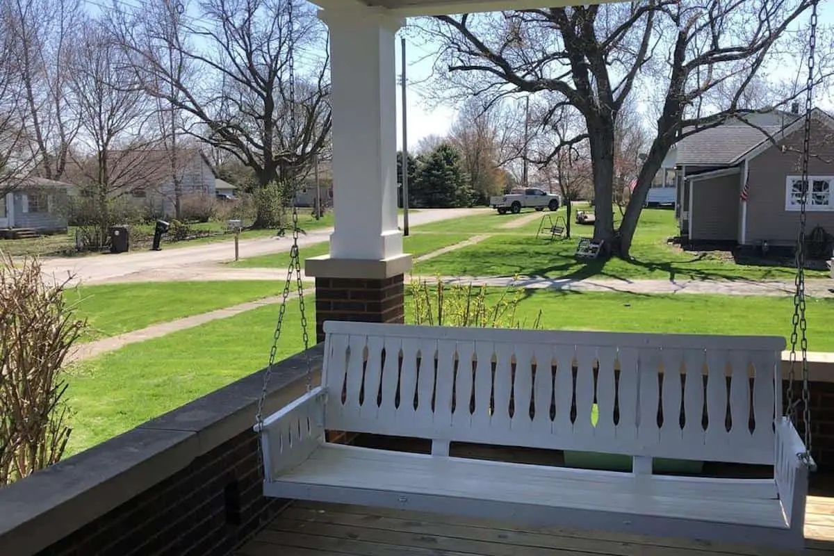 Photo of white porch swing on an American Foursquare style house. 