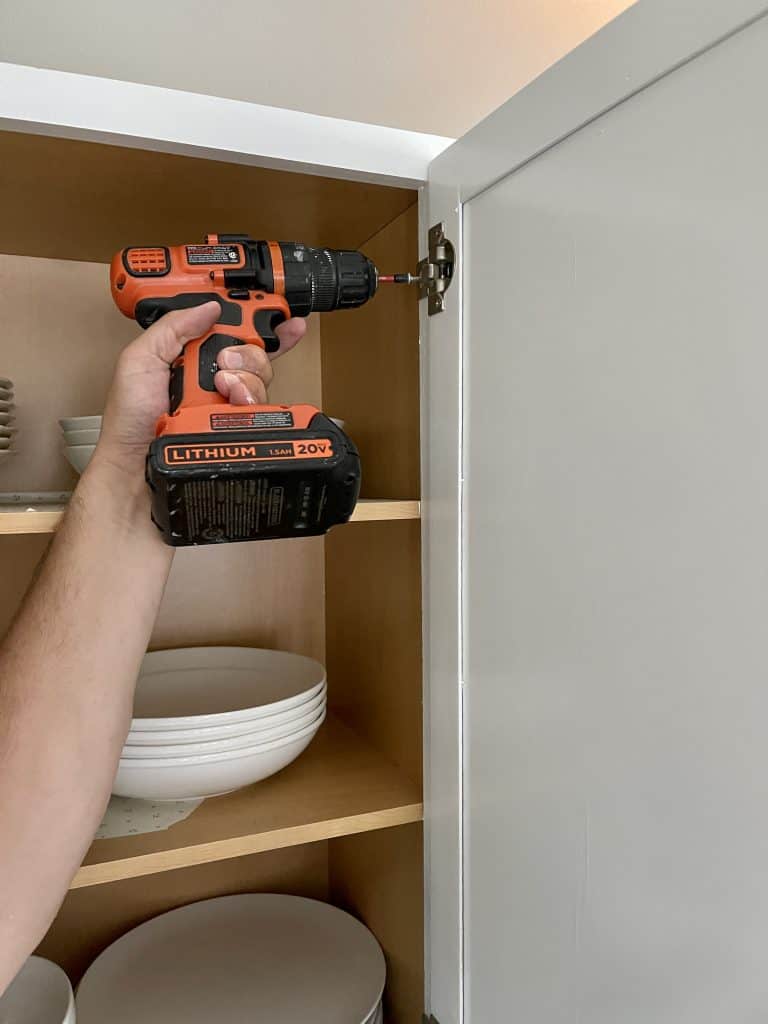 man's arm holding a drill to reattached cabinet door