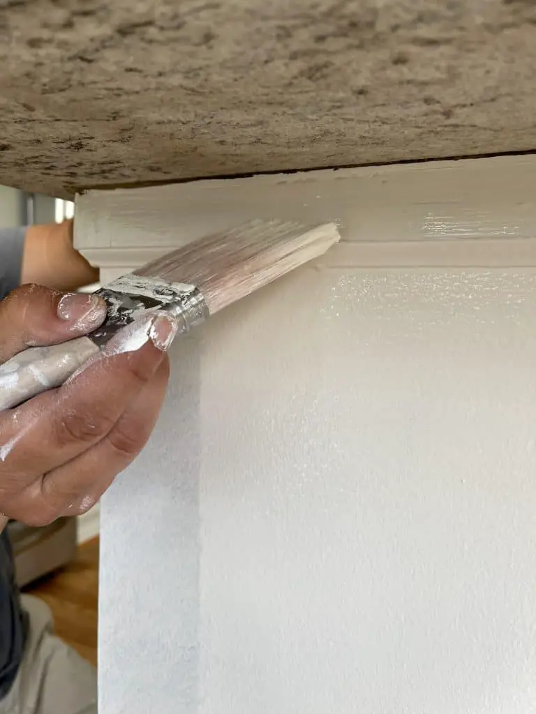 How to Paint Kitchen Cabinets that are Stained 25 hand holding paint brush with white paint