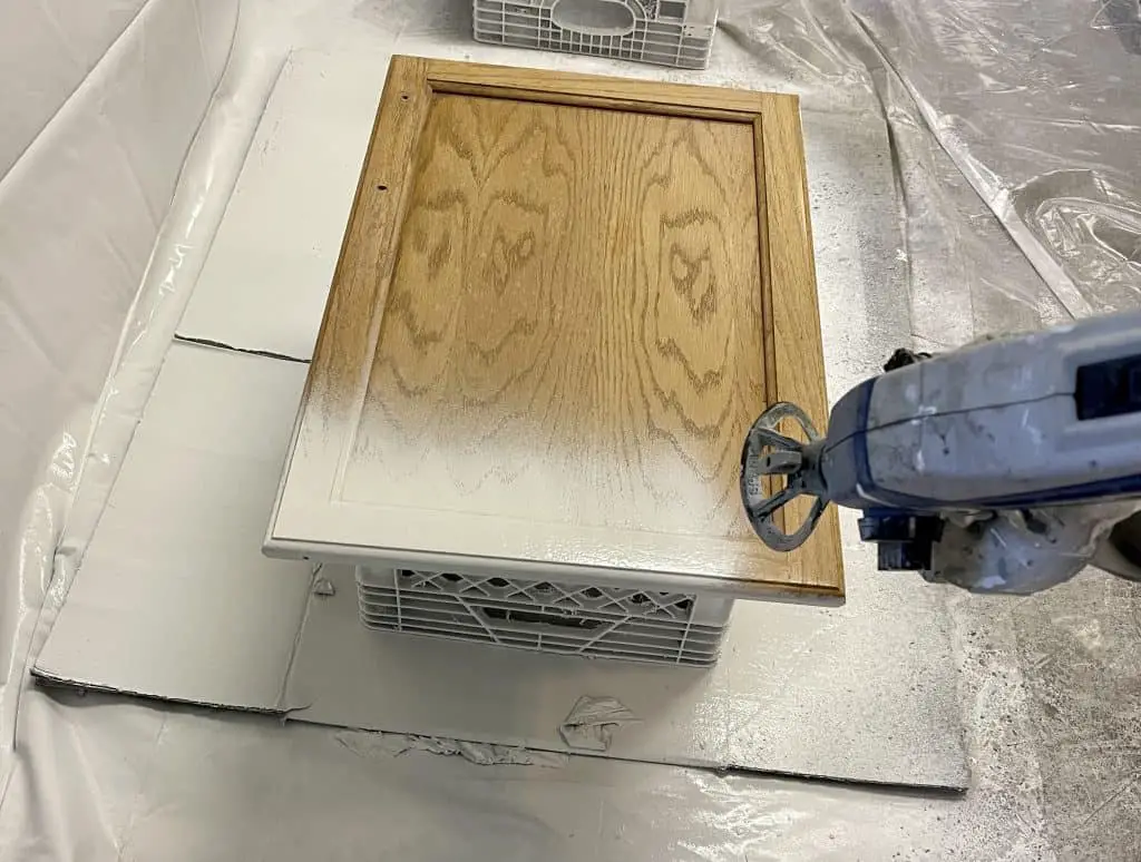 How to Paint Kitchen Cabinets that are Stained 20 paint sprayer painting a brown cabinet door white