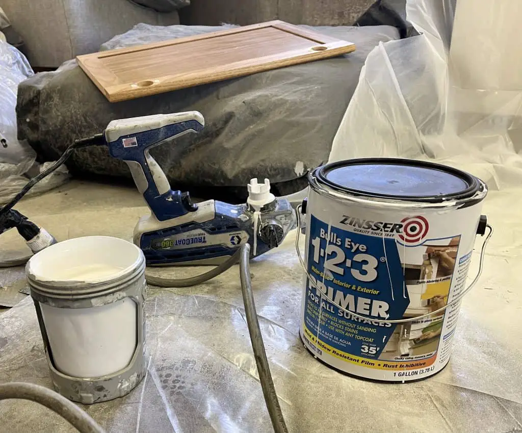 How to Paint Kitchen Cabinets that are Stained 18 can of white primer next to a spray gun